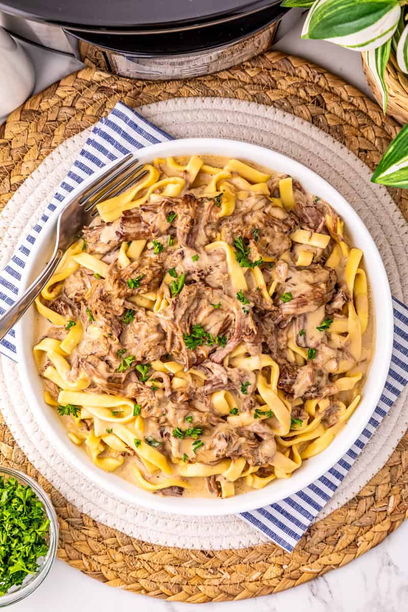 a bowl of slow cooker beef and noodles garnished with parsley.