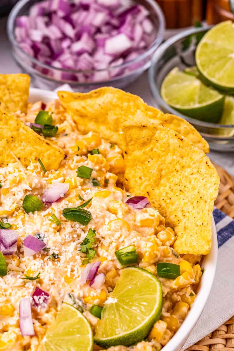 a bowl of slow cooker street corn dip with tortilla chips, jalapeno, red onion, and cilantro.