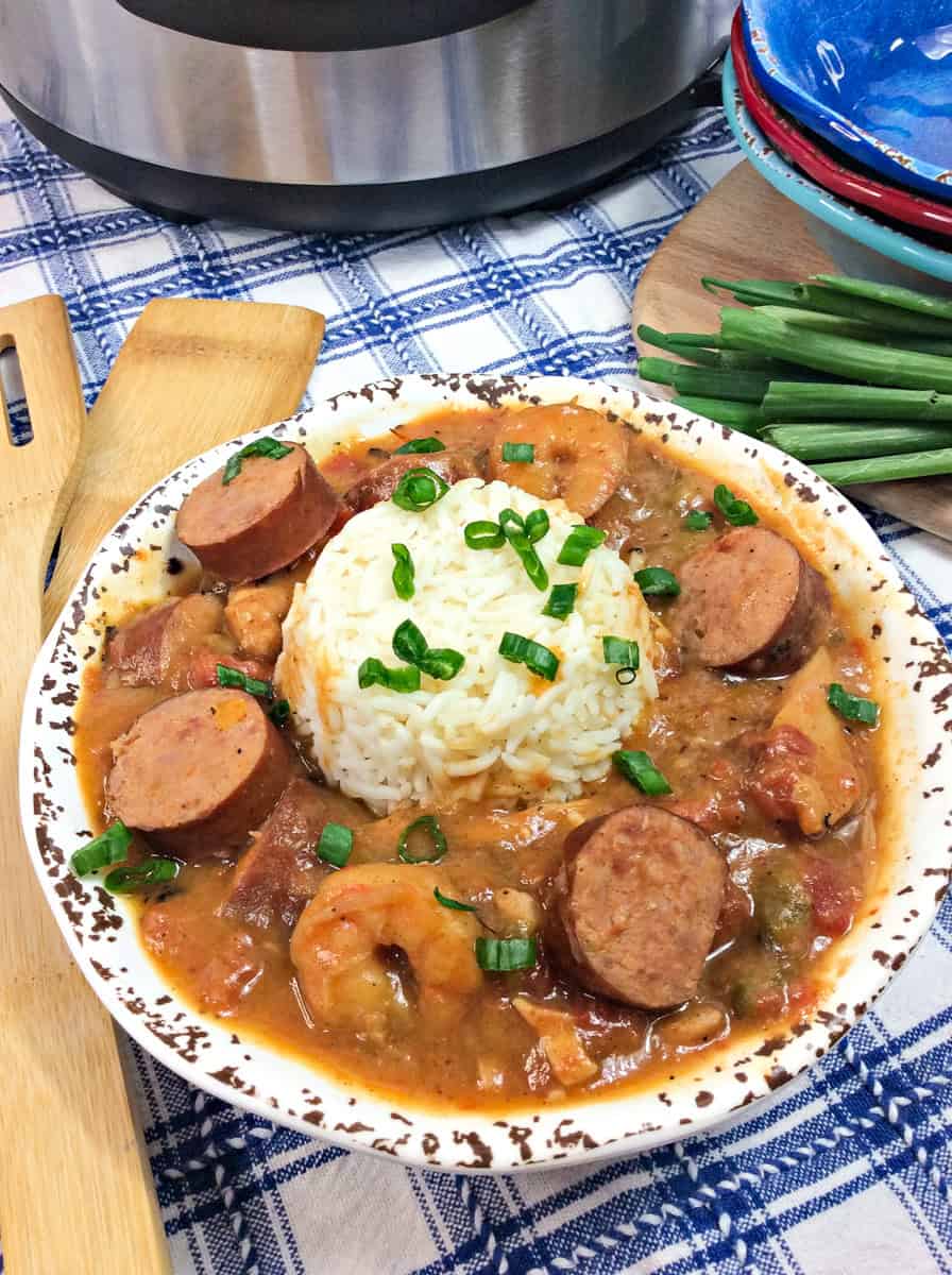 a bowl of sausage, chicken, and shrimp gumbo topped with rice, green onions, and parsley.
