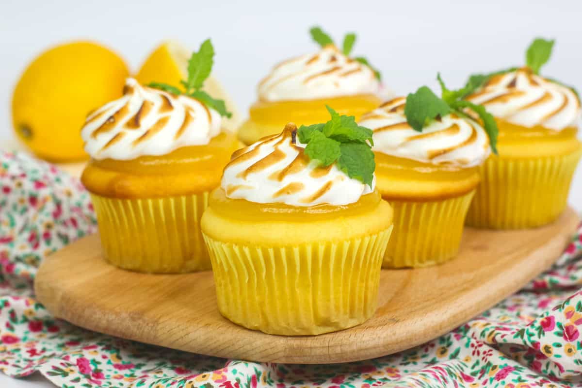 a wooden platter of lemon cupcakes topped with lemon curd and toasted meringue. 