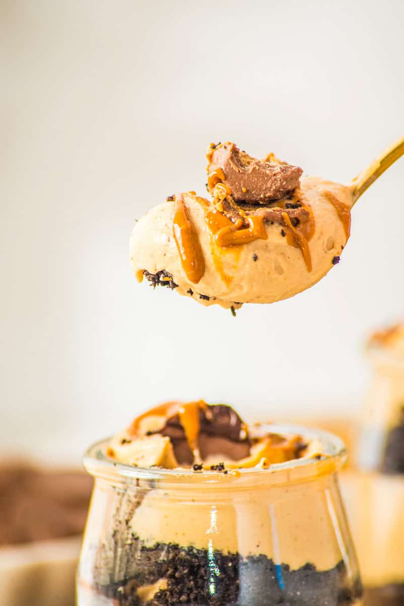 a closeup of a spoonful of peanut mousse drizzled with peanut butter and chocolate and topped with Reese's. 