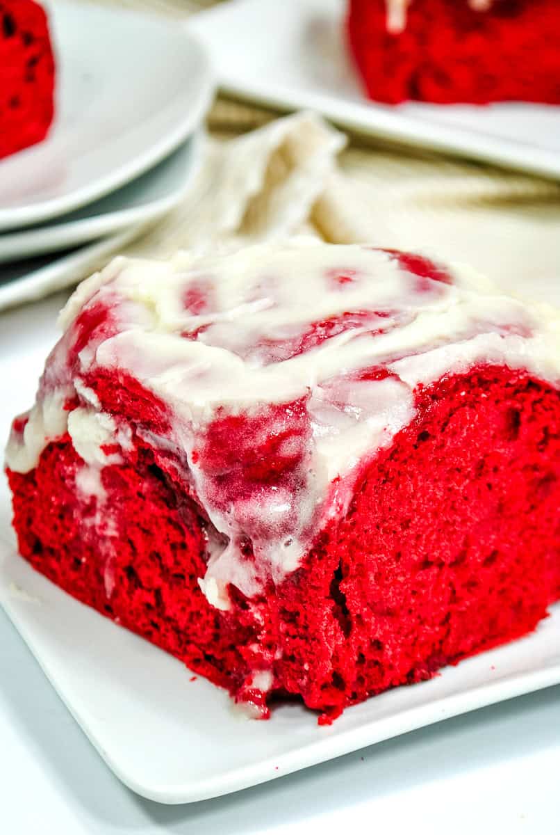 a closeup of a red velvet cinnamon roll topped with cream cheese frosting. 