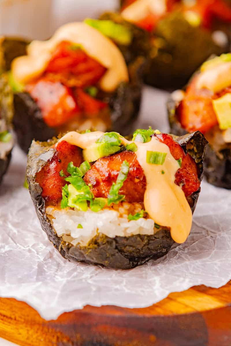 a nori sushi cup filled with rice and salmon and topped with green onions and spicy mayo.