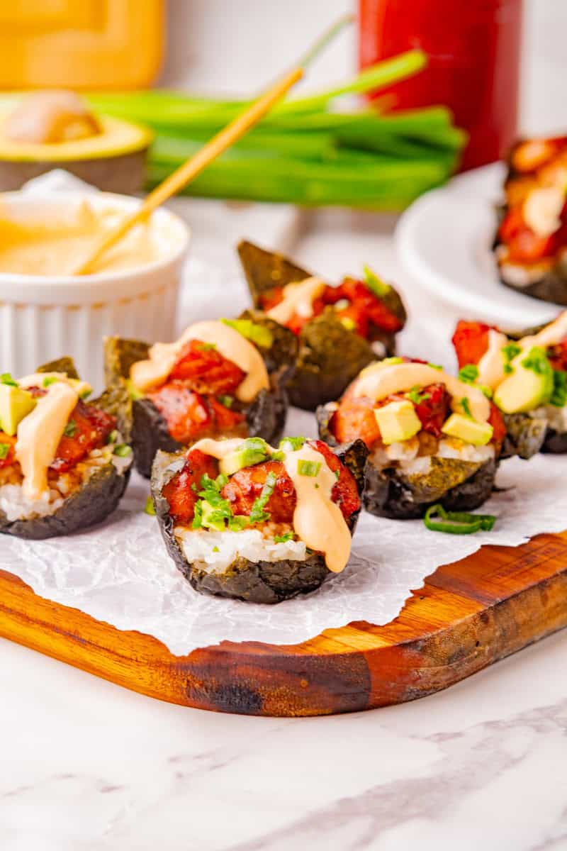 a wooden platter of salmon sushi cups with avocado, green onions, and spicy mayo.
