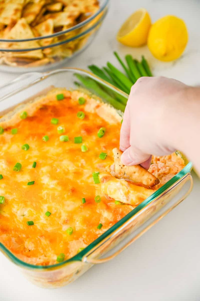 a pita cracker dipping into shrimp and crab dip topped with cheese and green onions.