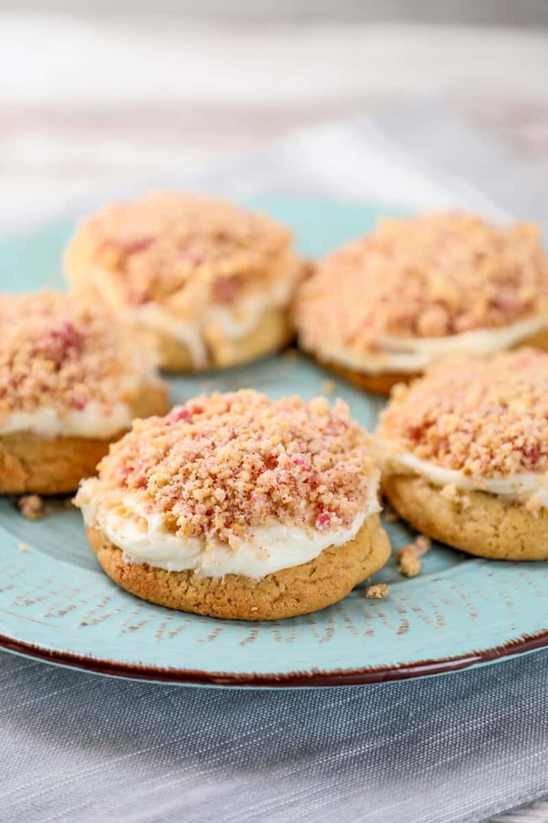 a plate of cookies topped with frosting and a strawberry shortcake crumble. 