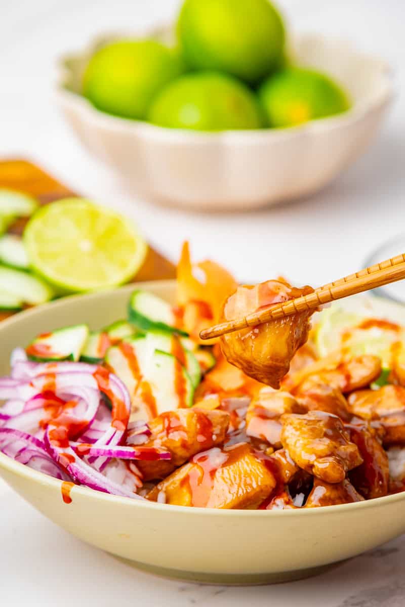 a poke bowl with teriyaki chicken, sliced cucumbers, red onion, and carrots with rice.