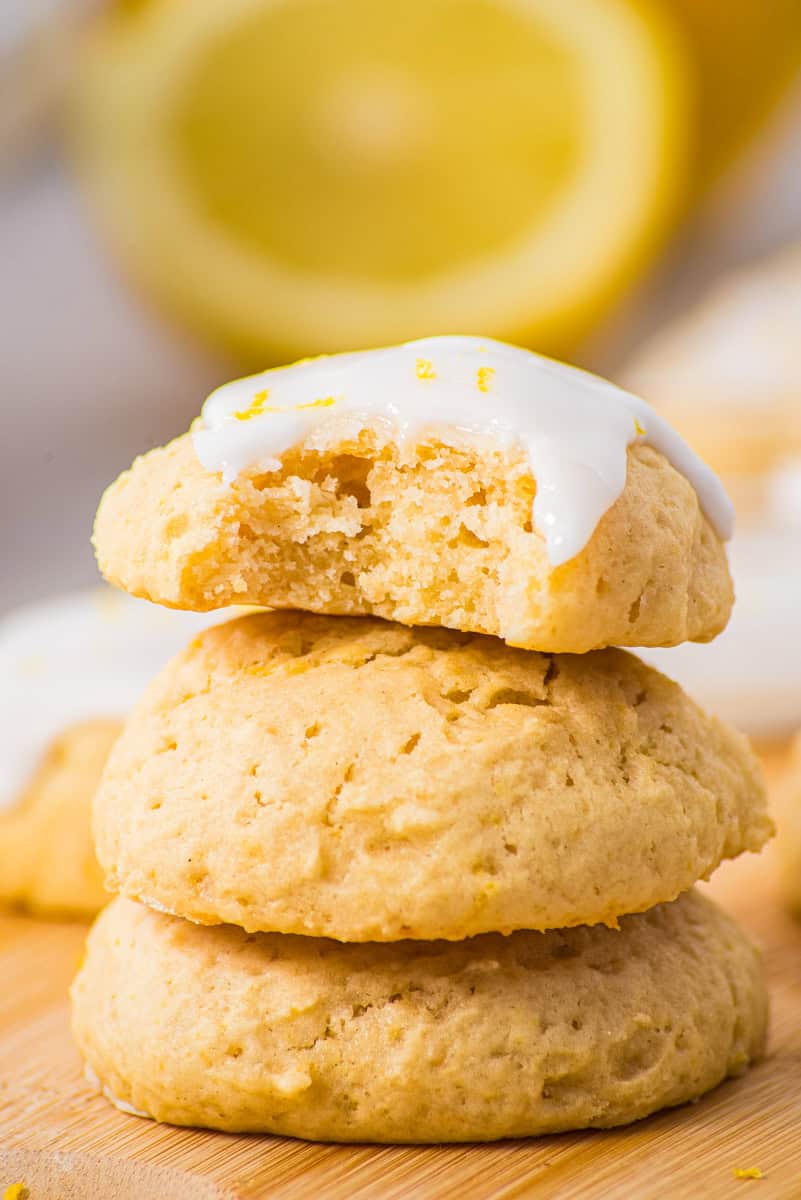 three lemon ricotta cookies stacked on top of each other with lemon glaze and lemon zest. 