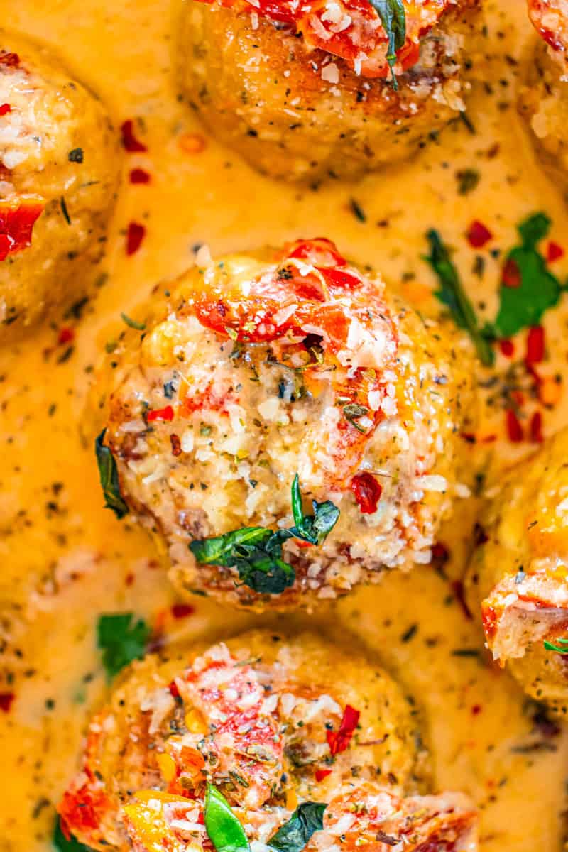 a marry me chicken meatballs with sundried tomatoes, parmesan cheese, and basil in a skillet with tomato cream sauce.