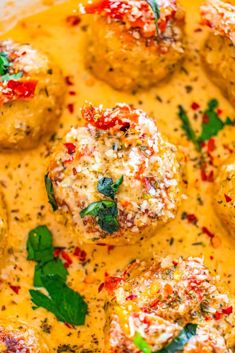 a closeup of a marry me meatballs with cheese and basil in a sundried tomato cream sauce.