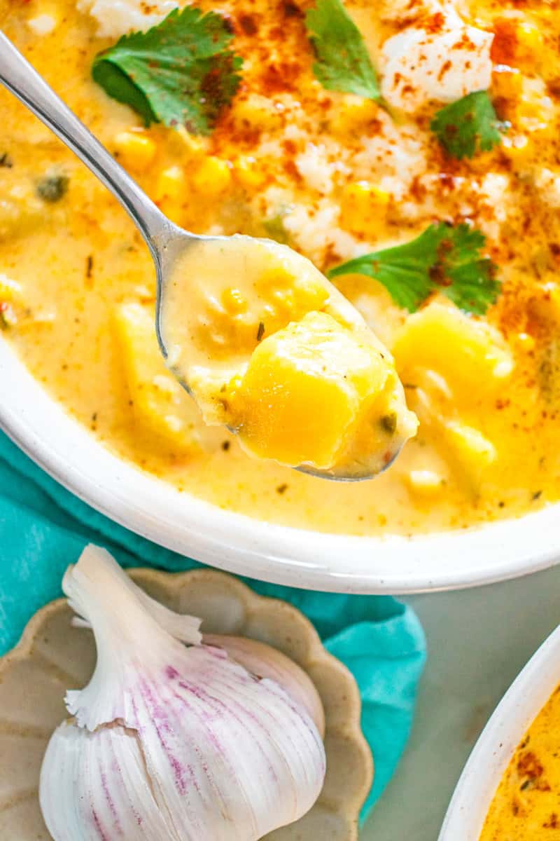 a spoon with street corn chowder with potatoes and corn.
