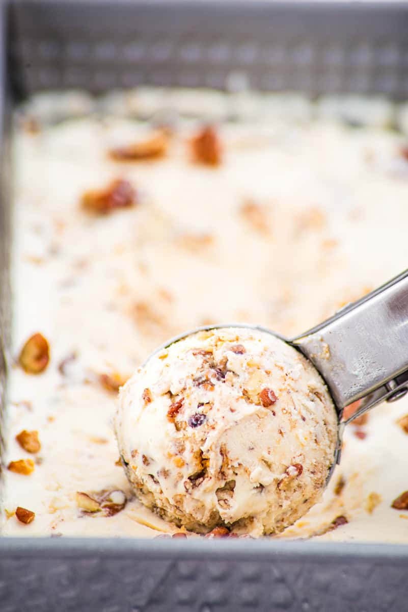 an ice cream scoop scooping out brown butter pecan ice cream from a loaf pan.