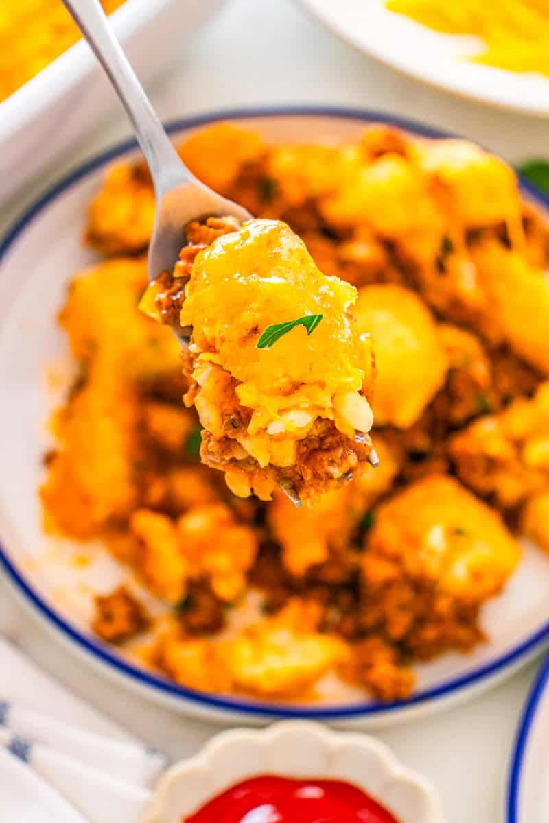 a fork with a bite of tater tot casserole with sloppy joes and cheese.