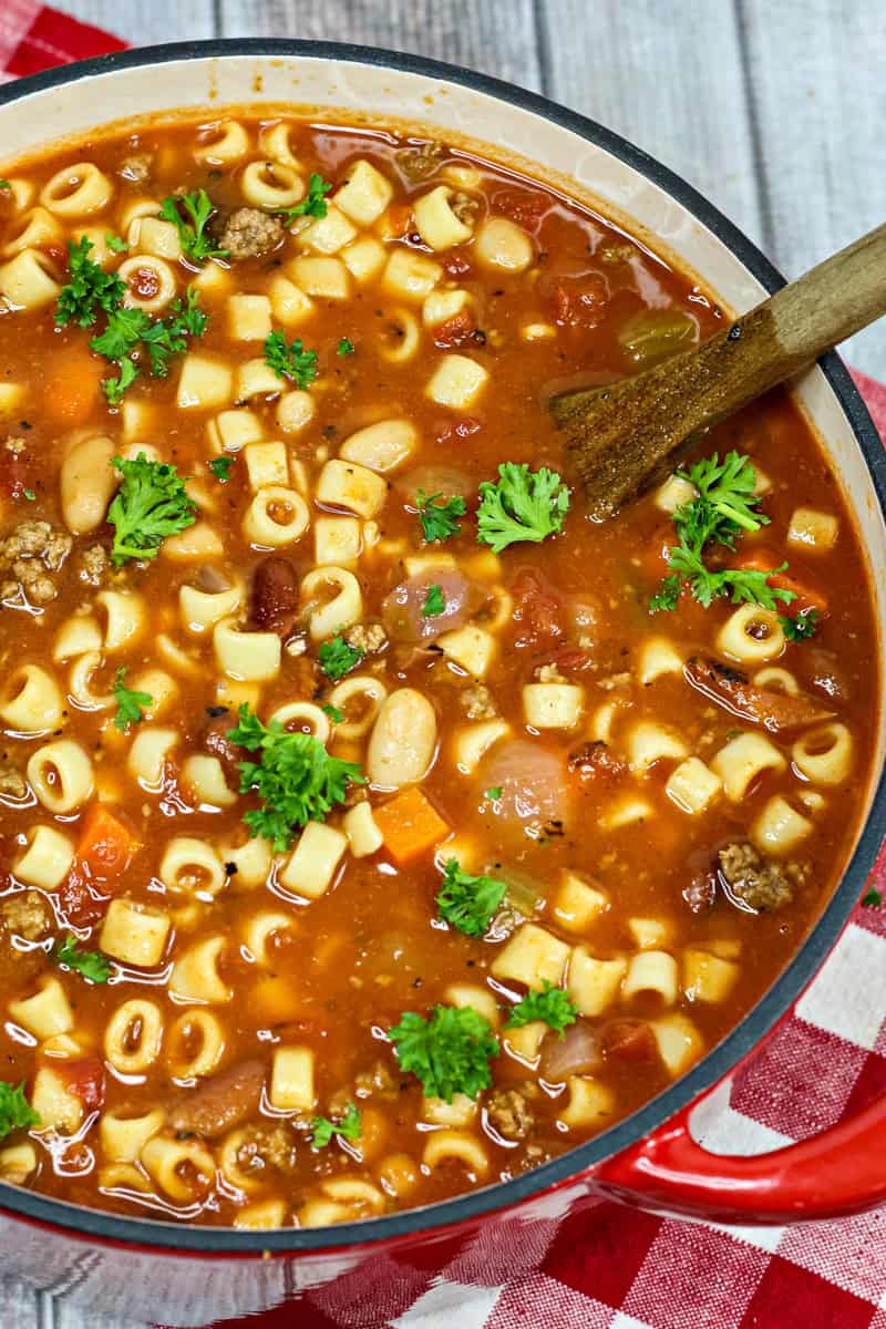 a pot full of pasta e fagioli with beans, carrots, pasta, beef, and garnished with parsley.