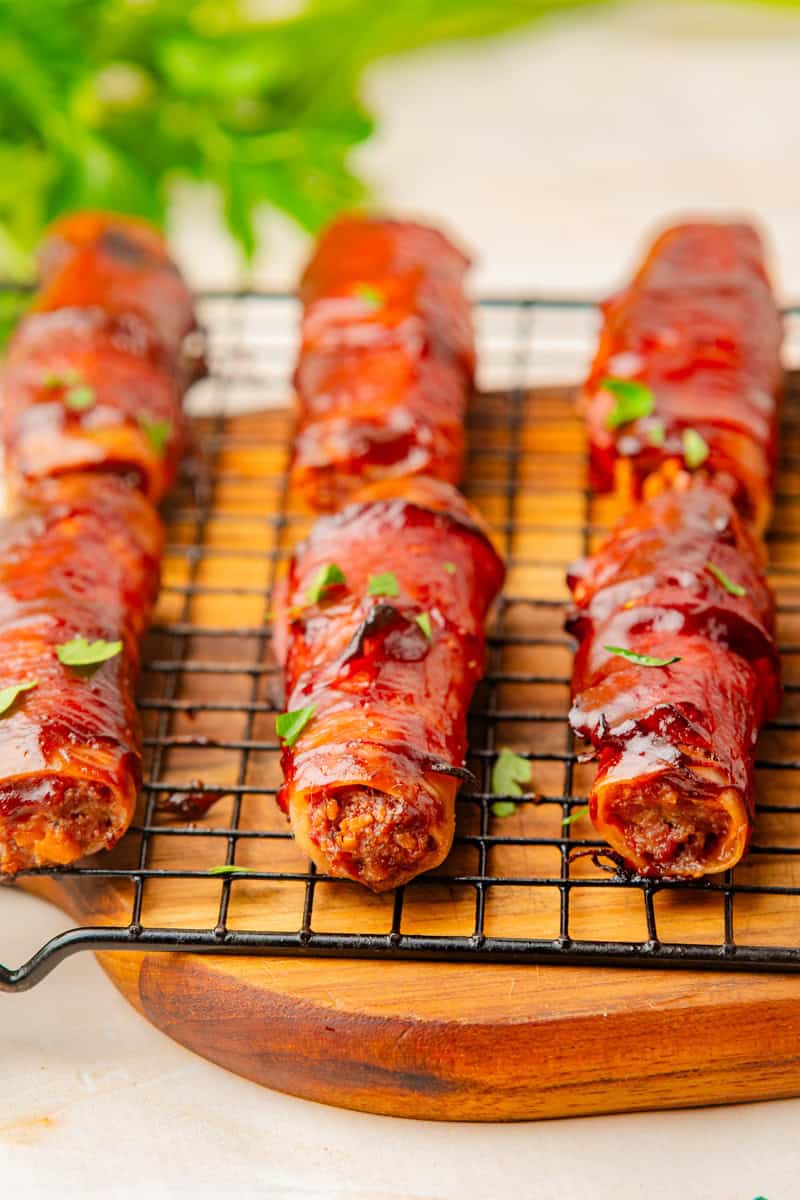 baked shotgun shells filled with beef and wrapped in bacon and brushed with BBQ sauce on a wire rack. 