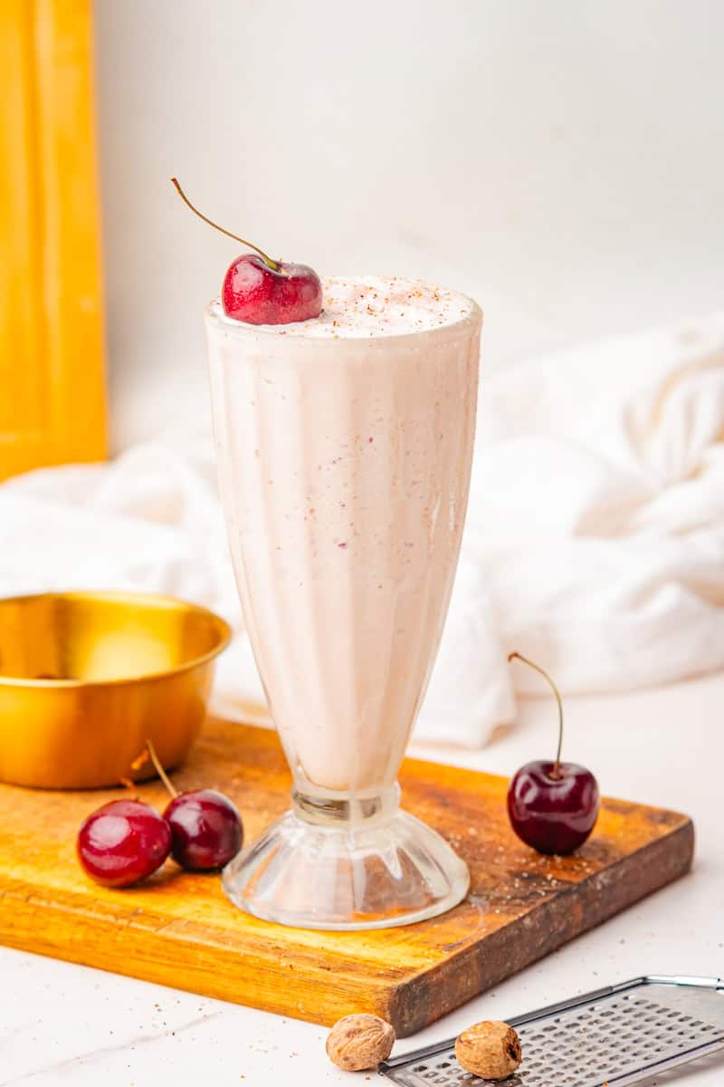 a Brandy Alexander milkshake in a tall glass garnished with nutmeg and a cherry. 