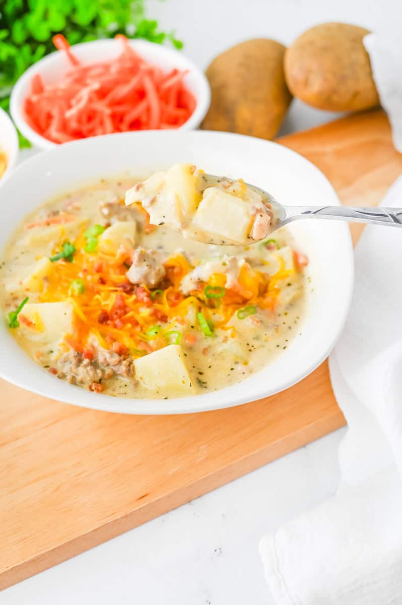 a bowl of cheeseburger soup with potatoes topped with bacon, cheese, and green onions.