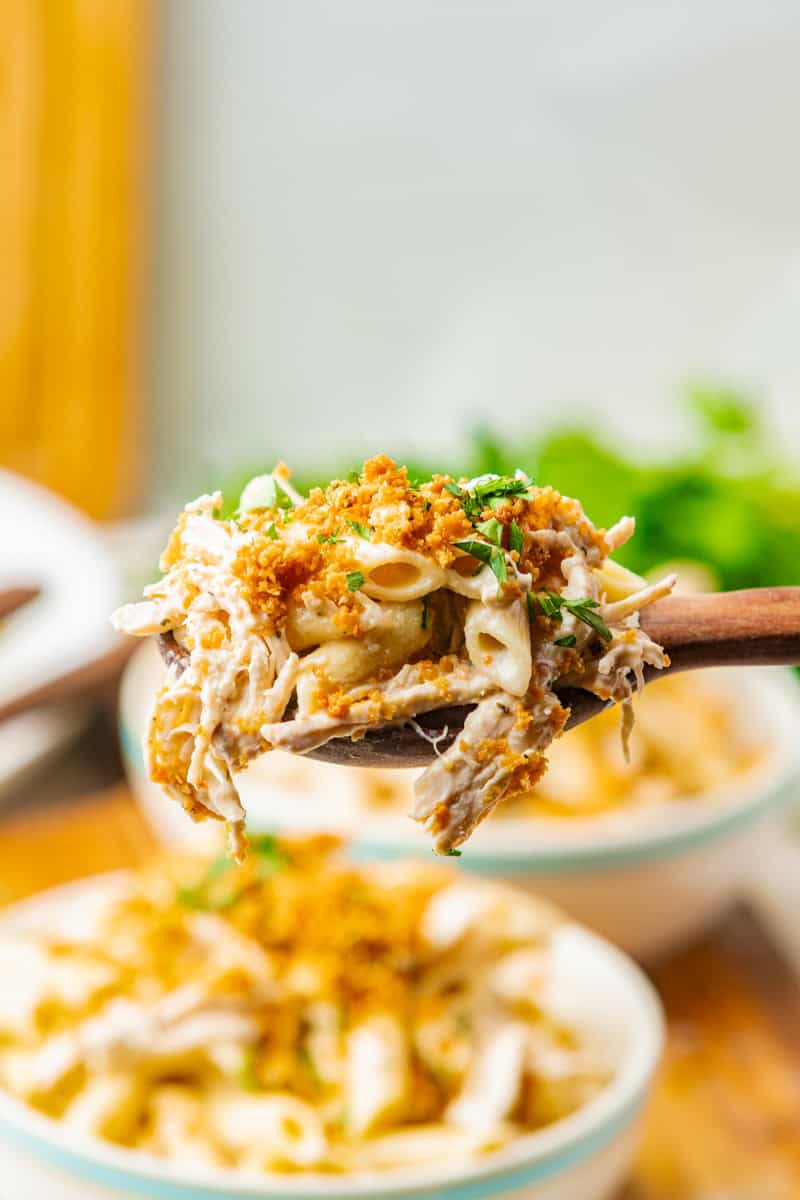 a wooden spoon lifting out a serving of olive garden crock pot pasta with chicken and bread crumbs.