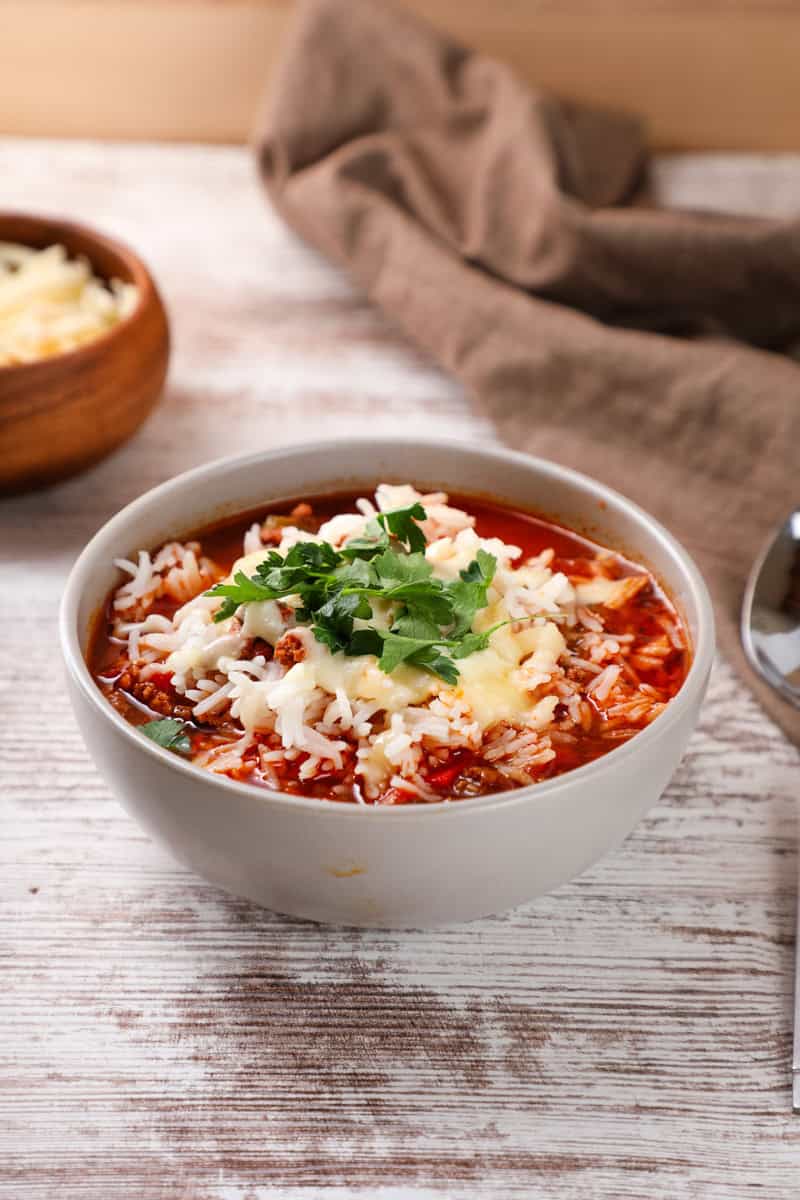 a bowl of slow cooker stuffed pepper soup with rice topped with mozzarella cheese and parsley.