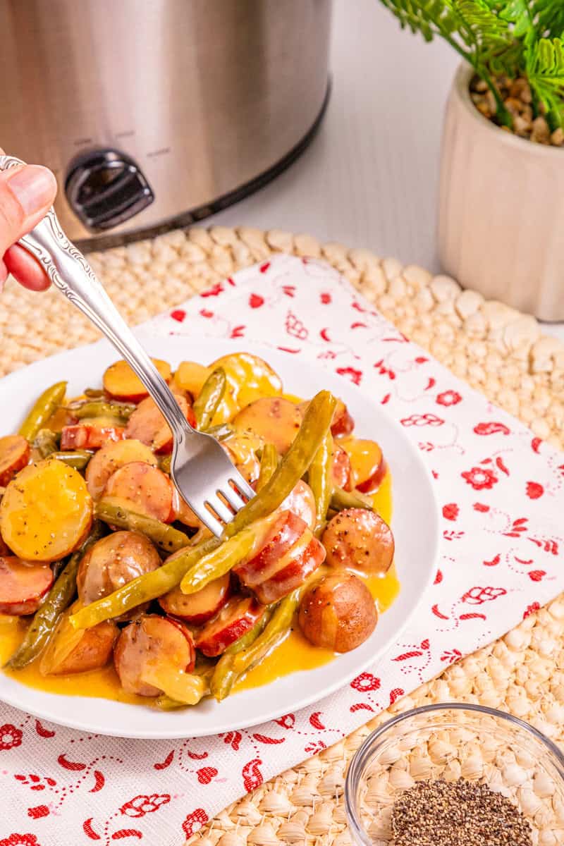 a fork picking up a serving of slow cooker swamp potatoes with green beans and sausage.
