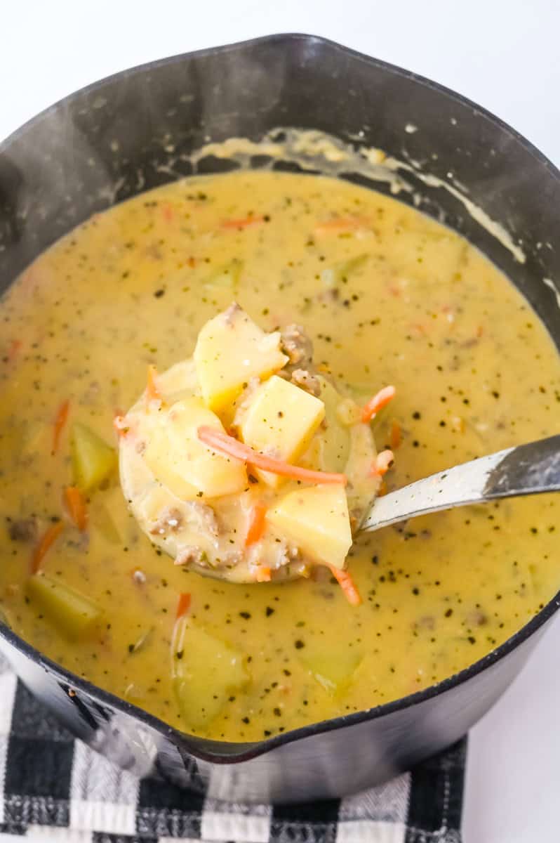 a ladle of cheeseburger soup with potatoes, carrots, ground beef, and a creamy broth.