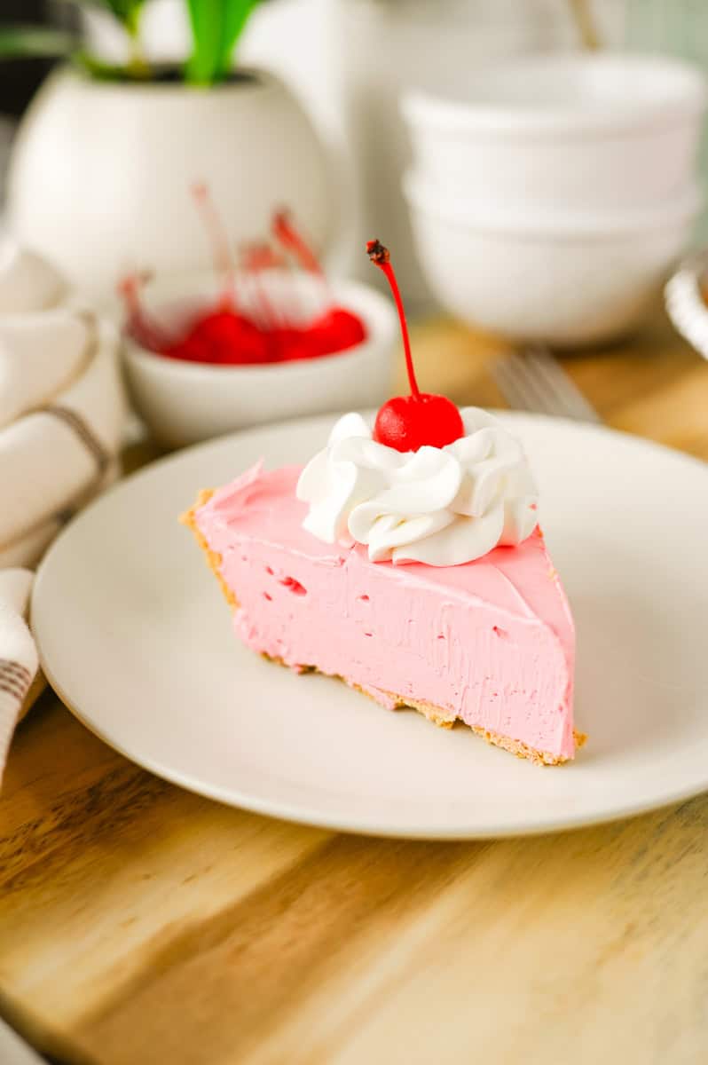 a slice of cherry Kool aid pie topped with whipped cream and a maraschino cherry. 