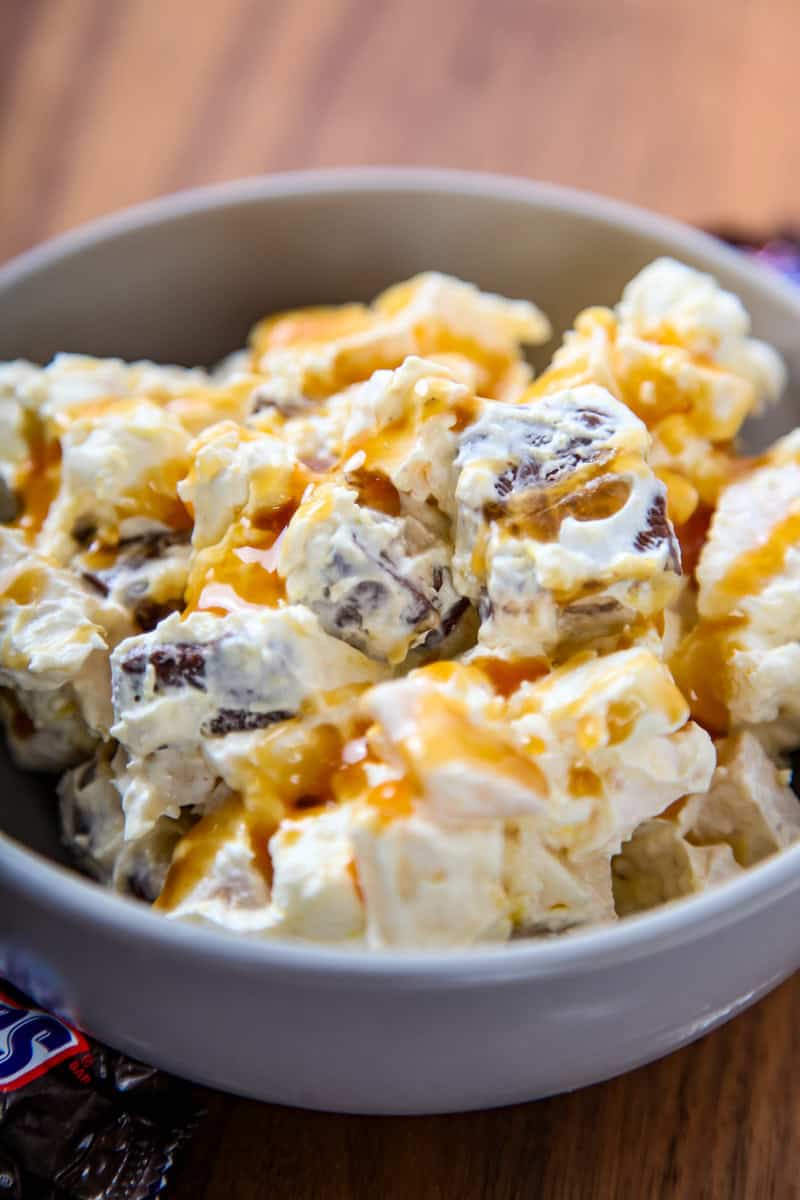 a bowl of Snickers salad with apples, caramel, marshmallows, and chopped Snickers candy bars.