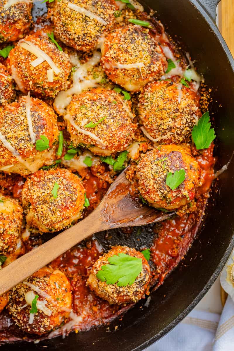 a wooden spoon lifting out a chicken parmesan meatball topped with panko, cheese, and parsley.