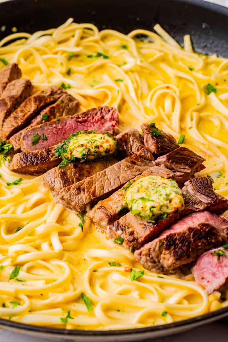a closeup of cowboy butter steak sliced on top of fettucine in a cream sauce.
