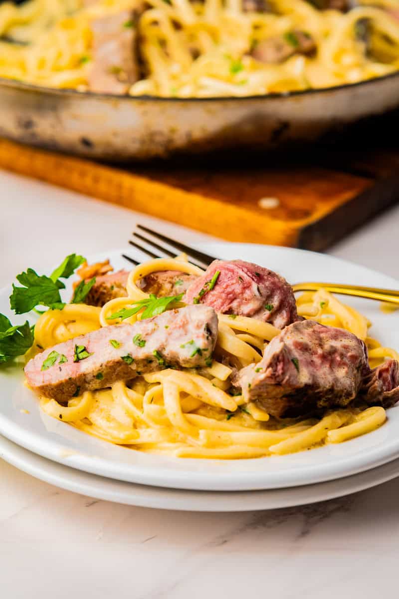 a plate of creamy steak pasta with sliced ribeye steak and parsley. 
