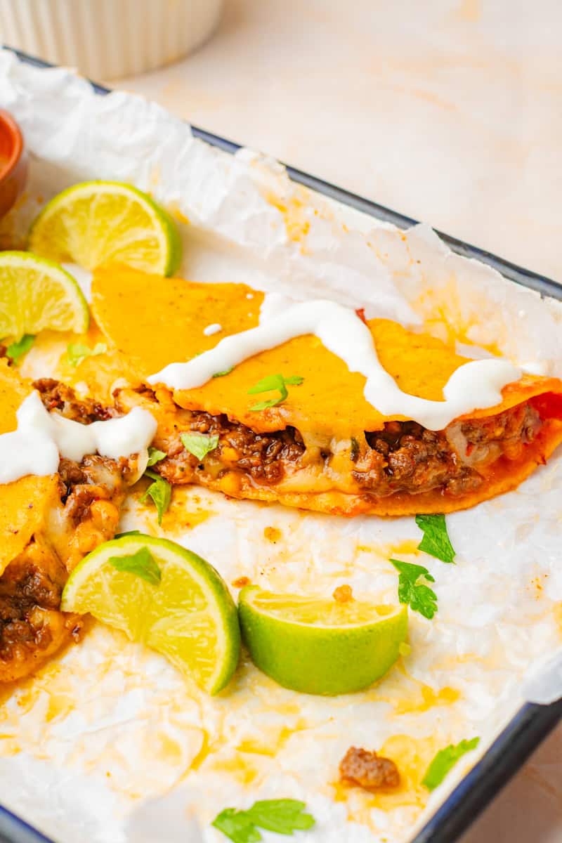 a sheet pan of crispy ground beef and cheese tacos topped with sour cream and cilantro.