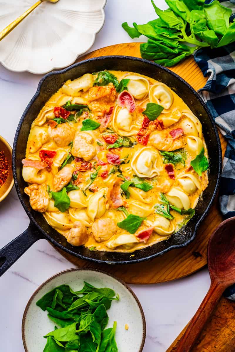a cast iron skillet of marry me chicken tortellini with spinach.