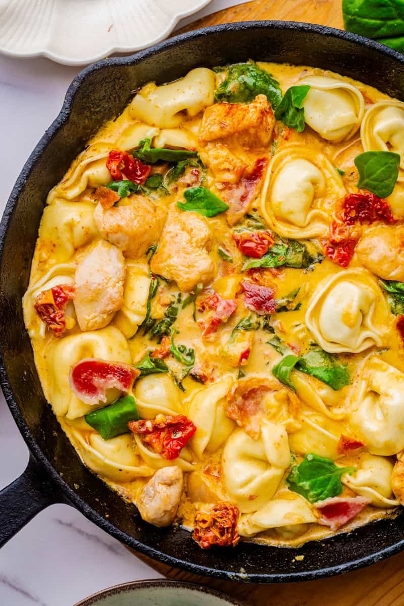 a skillet of tortellini with chicken and sundried tomatoes in a cream sauce.