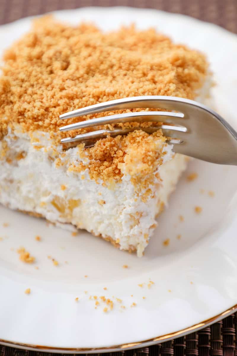 a fork cutting into a slice of pineapple dream dessert topped with graham cracker crumbs. 