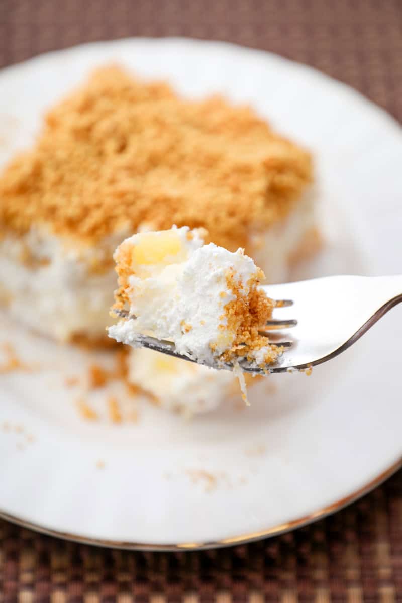 a bite of pineapple dream dessert with cream cheese and graham cracker crumbs on a fork.