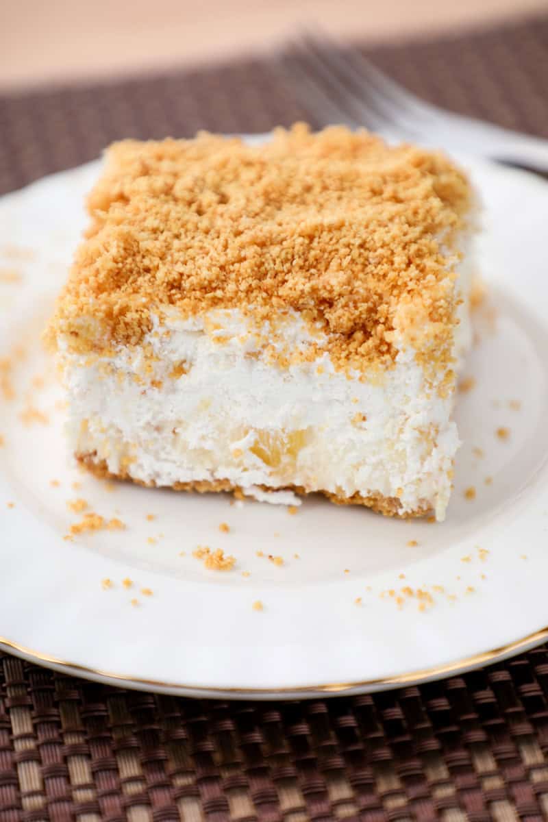 a slice of a graham cracker, cream cheese, and pineapple dessert on a white plate. 